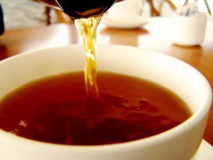 Black Tea is Red When Brewed Rich amber liquid pours and ripples into a white tea cup.