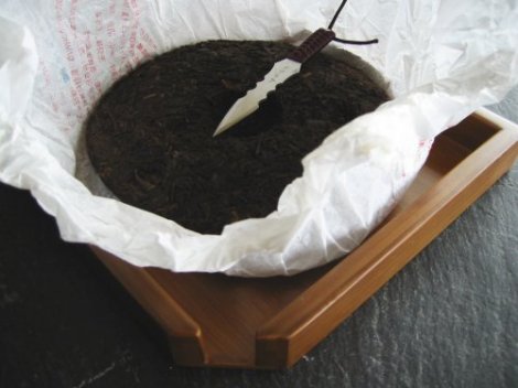 A pu-erh tea disc cake, which could be used to make tea, act as currency and represents wealth, sits on a white piece of tissue paper with a knife.