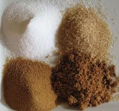 Four piles of different types of sugar on a table: White Sugar, Evaporated Cane Juice, Brown Sugar & Demerrera.