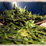 Green tea leaves spill from a roaster