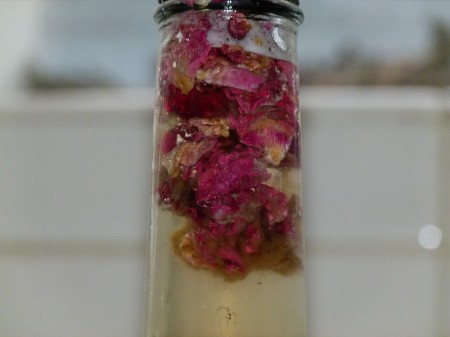 A close up of brown yeast strands mixing with rose petal flavorings in the neck of a Hannah's Homebrew Kombucha bottle.