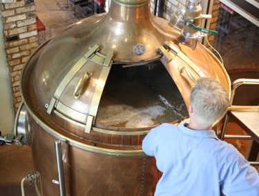 A large brass beer brewing vessel is tended
