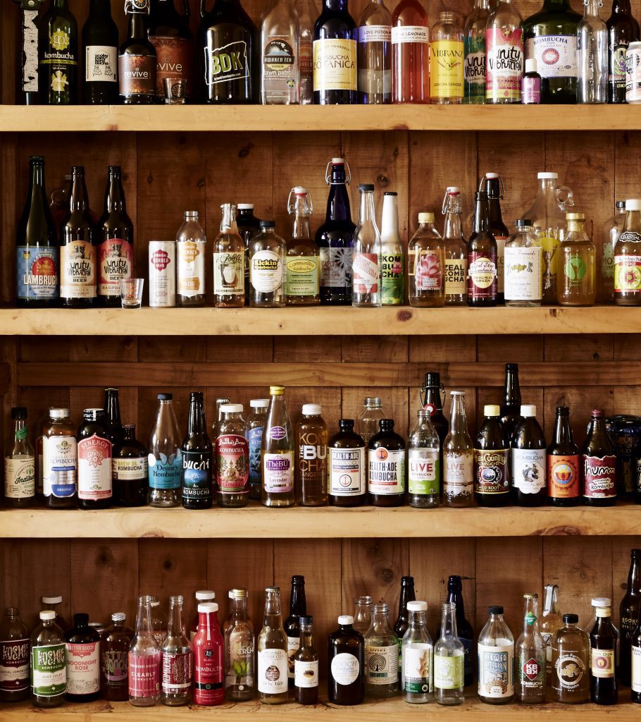 wooden bookshelf holds several bottles of Kombucha from many different brands - called a "Kombucha Museum"